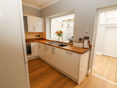 A kitchen with white cabinets wooden countertops a sink and a window with flowers at Grace House in Silloth