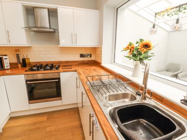 A kitchen with wooden countertops white cabinets a stove and an oven a sink with a dish rack and sunflowers in a vase by a window at Grace House in Silloth