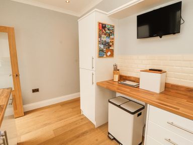 A kitchen corner with white cabinets a wooden countertop a mounted television and a double trash bin at Grace House in Silloth