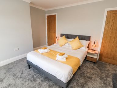 A bedroom with a double bed yellow pillows and folded towels on a bed runner at Grace House in Silloth