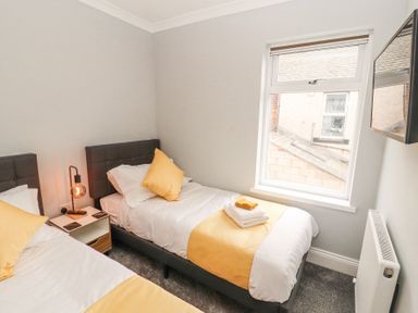 A bedroom with two single beds a bedside table a lamp and a wall-mounted television at Grace House in Silloth
