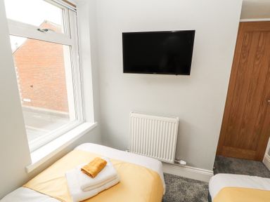 A bedroom with two single beds next to a window a radiator a wall-mounted TV and a wooden door at Grace House in Silloth