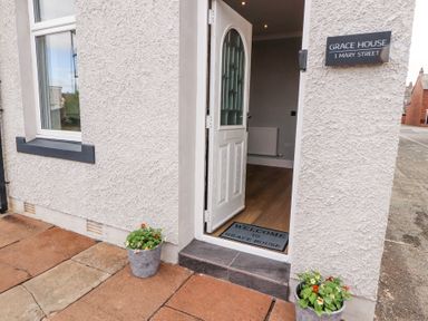 An open white door showing a welcome mat and flower pots outside at Grace House in Silloth
