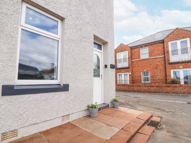 A building entrance with a white door and window with pots on either side at Grace House in Silloth