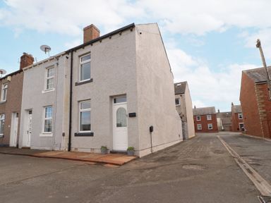 A row of terraced houses on a street with a grey end house and a narrow road beside it at Grace House in Silloth