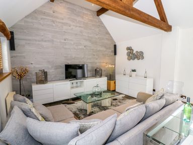 A living room with a gray sofa a glass coffee table and a TV on a white cabinet at The Bit on the Side in Ettington
