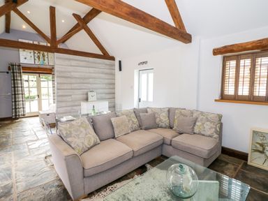 A living room with a gray sectional sofa and wooden beams on the ceiling at The Bit on the Side in Ettington