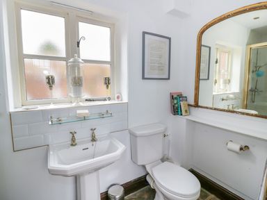 A bathroom with a sink toilet mirror and window with decorative items at The Bit on the Side in Ettington
