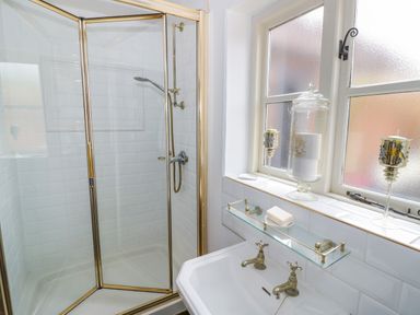 A bathroom with a shower enclosure a sink with dual taps and candles on the windowsill at The Bit on the Side in Ettington