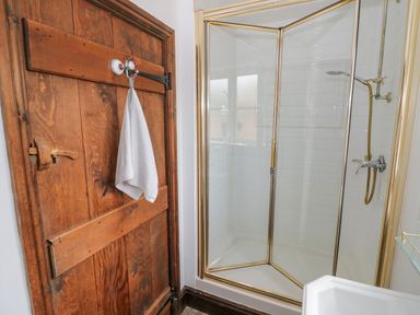 A bathroom with a wooden door with a white towel hanging and a corner shower with glass doors at The Bit on the Side in Ettington