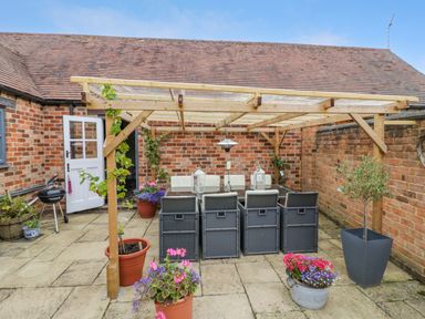 A patio with a wooden pergola over a dining table and chairs surrounded by potted plants at The Bit on the Side in Ettington