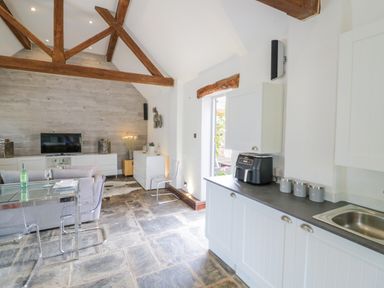 An open living room and kitchen area with wooden beams and glass chairs at The Bit on the Side in Ettington