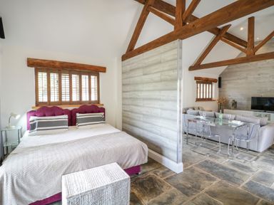 A bedroom with a bed and a wicker chest next to a living area with a sofa and glass dining table at The Bit on the Side in Ettington