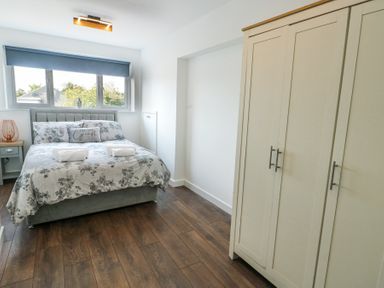 A bedroom with a double bed with floral bedding two towels on the bed a bedside table with a lamp and a wardrobe at Ty Copr in Amlwch