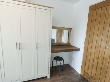 A room corner with a white wardrobe a wooden floating desk with a mirror and a black stool at Ty Copr in Amlwch