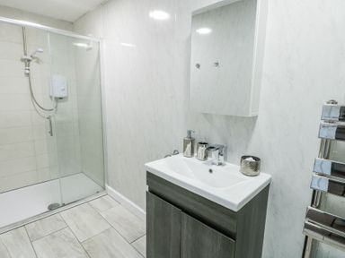 A bathroom with a glass enclosed shower on the left a sink with a cabinet and a wall mirror above at Ty Copr in Amlwch
