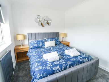 A bedroom with a bed with blue floral bedding two bedside tables with lamps and a decorative mirror on the wall at Ty Copr in Amlwch