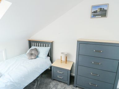 A bedroom with a single bed a bedside table with a lamp a chest of drawers and a framed picture on the wall at Ty Copr in Amlwch