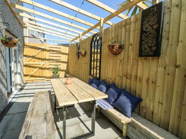 An outdoor seating area with a wooden table and benches under a wooden pergola at Ty Copr in Amlwch