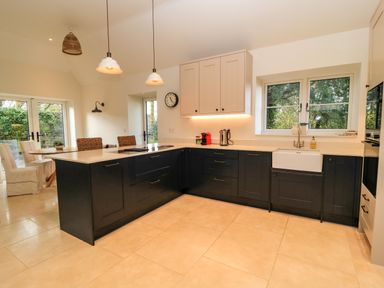A kitchen with black lower cabinets and beige upper cabinets a farmhouse sink and dining table with chairs at The Elm Coach House in Chipping Norton