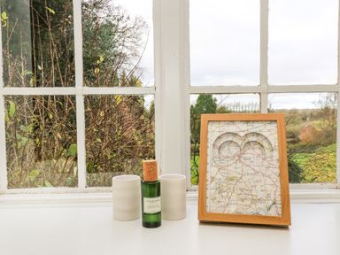 A window sill with two white containers a green bottle and a framed map at The Elm Coach House in Chipping Norton