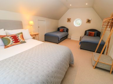 A bedroom with one double bed and two single beds under a sloped ceiling at The Elm Coach House in Chipping Norton