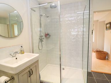 A bathroom with a sink and mirror next to a shower with glass doors and white tiles at The Elm Coach House in Chipping Norton