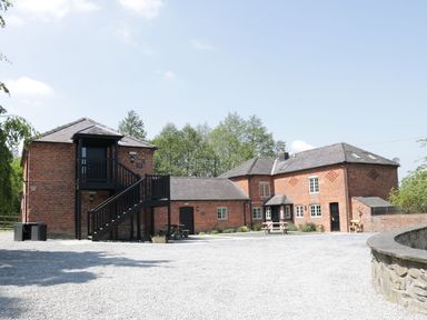 A gravel courtyard with brick buildings and black wooden staircases surrounded by trees at Woodside Cottage in Kerry