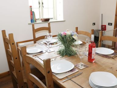 A wooden dining table set with plates wine glasses cutlery and a floral centerpiece at Woodside Cottage in Kerry