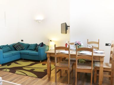 A living area with a teal corner sofa and wooden dining table set with plates and flowers at Woodside Cottage in Kerry