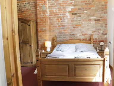 A bedroom with a wooden bed, bedside tables, lamps, and a wooden wardrobe against a brick wall at Woodside Cottage in Kerry