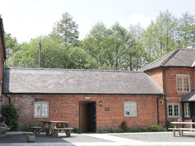An outdoor area with two picnic tables in front of a brick building with windows at Woodside Cottage in Kerry