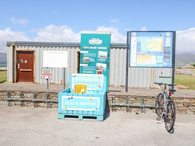 A bike parked next to a blue beach borrow box and informational signs in front of a metal building at Knockbrack in Lonart near Killorglin County Kerry