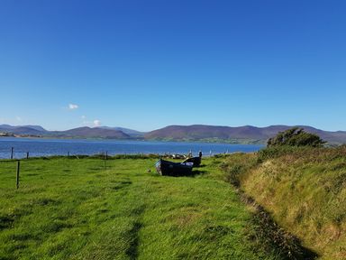 A grassy field with two boats near a body of water and mountains in the background at Knockbrack Lonart near Killorglin County Kerry