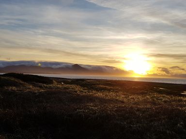A sunset over a body of water with mountains and grassy land at Knockbrack Lonart near Killorglin County Kerry