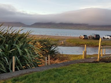 A grassy area with shrubs and a fence overlooking a lake with parked cars and mountains in the background at Knockbrack Lonart near Killorglin County Kerry