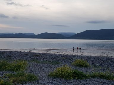 A rocky shore with three people walking near the water and mountains in the background at Knockbrack Lonart near Killorglin County Kerry