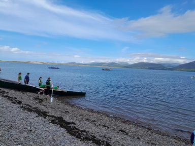 People preparing a canoe on a rocky shore with water and mountains in the background at Knockbrack Lonart near Killorglin County Kerry