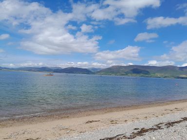A beach with sand and pebbles next to a body of water with mountains in the background at Knockbrack in Lonart near Killorglin County Kerry