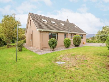 A beige house with a sloped roof and four skylights surrounded by green lawn and bushes at Knockbrack Lonart near Killorglin County Kerry
