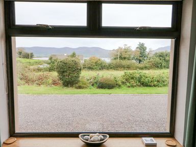 A window with a bowl of stones and other items on the sill overlooking a garden and mountains at Knockbrack Lonart near Killorglin County Kerry