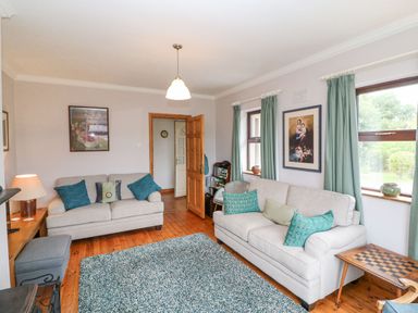 A living room with two beige sofas and blue cushions a checkered table two windows with green curtains and paintings on the wall at Knockbrack Lonart near Killorglin County Kerry