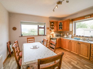 A kitchen with wooden cabinets a dining table and chairs and large windows at Knockbrack Lonart near Killorglin County Kerry
