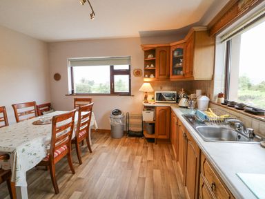 A kitchen with wooden cabinets a sink a dining table with chairs and windows at Knockbrack in Lonart near Killorglin County Kerry