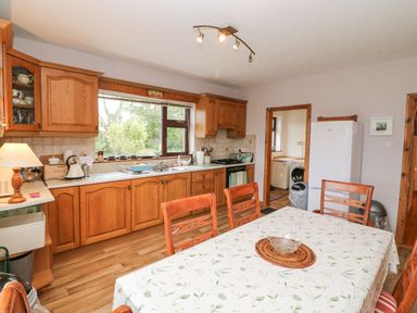 A kitchen with wooden cabinets a dining table with chairs and a white refrigerator at Knockbrack Lonart near Killorglin County Kerry