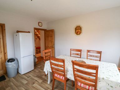 A dining area with wooden chairs around a table covered with a tablecloth and a refrigerator in the corner at Knockbrack in Lonart near Killorglin County Kerry
