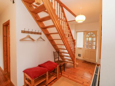 An entryway with wooden stairs a bench with red cushions a chair coat hooks and a door at Knockbrack Lonart near Killorglin County Kerry