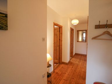 A hallway with wooden doors wooden floor a small table with a lamp a mirror on the wall and a wooden coat rack with a hanger at Knockbrack Lonart near Killorglin County Kerry