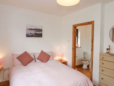 A bedroom with a bed pillows bedside tables lamps a dresser and an ensuite bathroom at Knockbrack in Lonart near Killorglin County Kerry