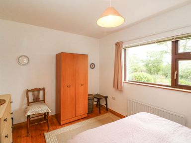 A bedroom with a wooden wardrobe a chair a window with curtains and a bed at Knockbrack Lonart near Killorglin County Kerry